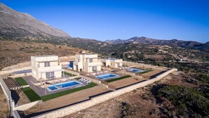 Une villa moderne dotée de deux piscines, d’un mur de soutènement en pierre et offrant une vue sur les collines environnantes.