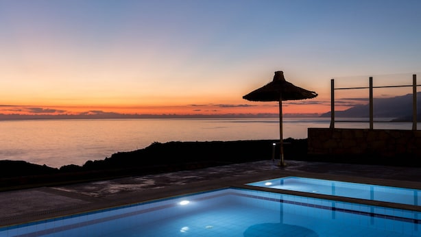 Une piscine avec vue sur l’océan au coucher du soleil.