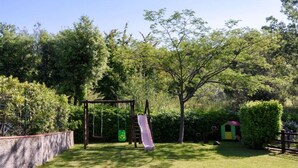 A playground with a slide and swings, surrounded by a hedge and trees.