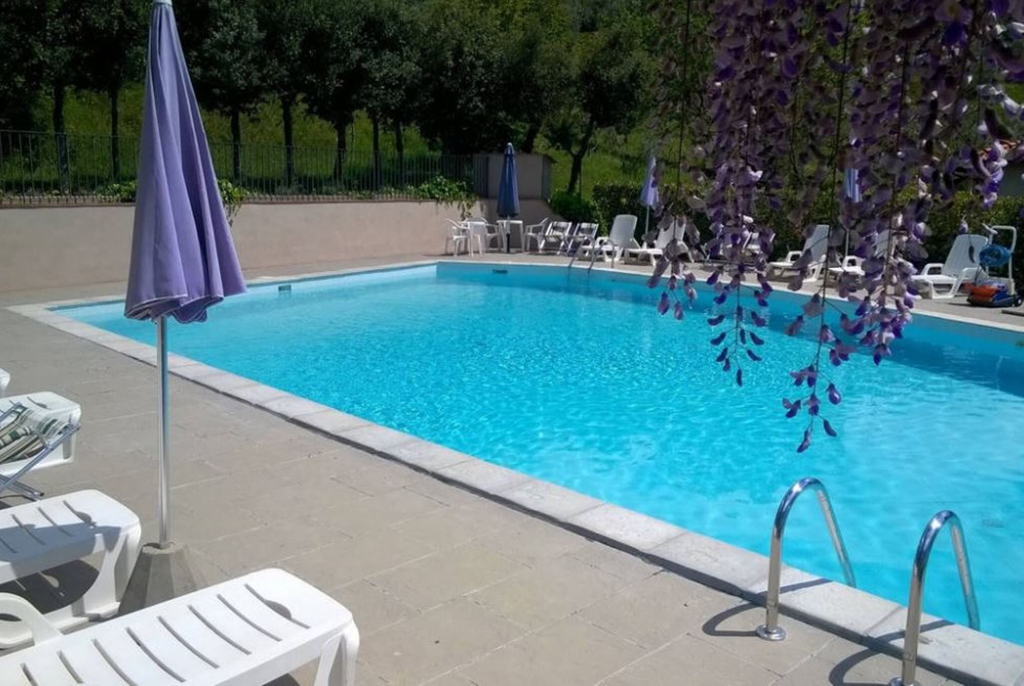 Una piscina con agua azul cristalina, rodeada de sillas reclinables blancas y un paraguas morado.