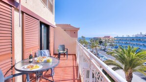 A balcony with a table set for two, a chair, and a bottle of champagne. The balcony overlooks a street with palm trees and a blue building in the background. - LOVELY 2 BEDROOMED APARTMENT NEXT TO THE BEACH (Arona)