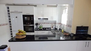 A modern kitchen with white cabinets, a black countertop, a refrigerator, an oven, and a kettle. - Town House With Private Pool ,Good WiFi. Short walk to Villamartin Plaza (alicante)