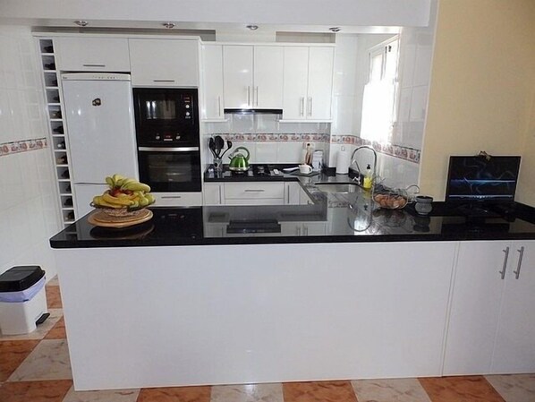 A modern kitchen with white cabinets, a black countertop, a refrigerator, an oven, and a kettle.