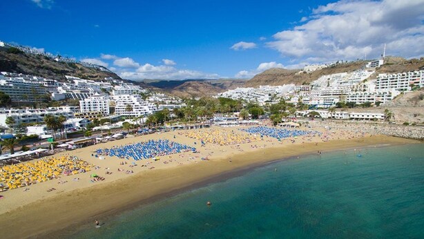A coastal area with a sandy beach, numerous umbrellas, and buildings in the background. - "🏖 Double terrace with sun all day - 2 bedrooms - Perfect for 4 - Mogán (Mogán)
