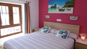A bedroom with a bed, a window with curtains, a wall-mounted picture, bedside lamps, and a bedside table with a candle. - "🏖 Double terrace with sun all day - 2 bedrooms - Perfect for 4 - Mogán (Mogán)