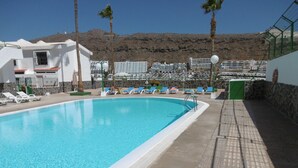 A swimming pool with lounge chairs and a view of a mountainous landscape in the background. - "🏖 Double terrace with sun all day - 2 bedrooms - Perfect for 4 - Mogán (Mogán)