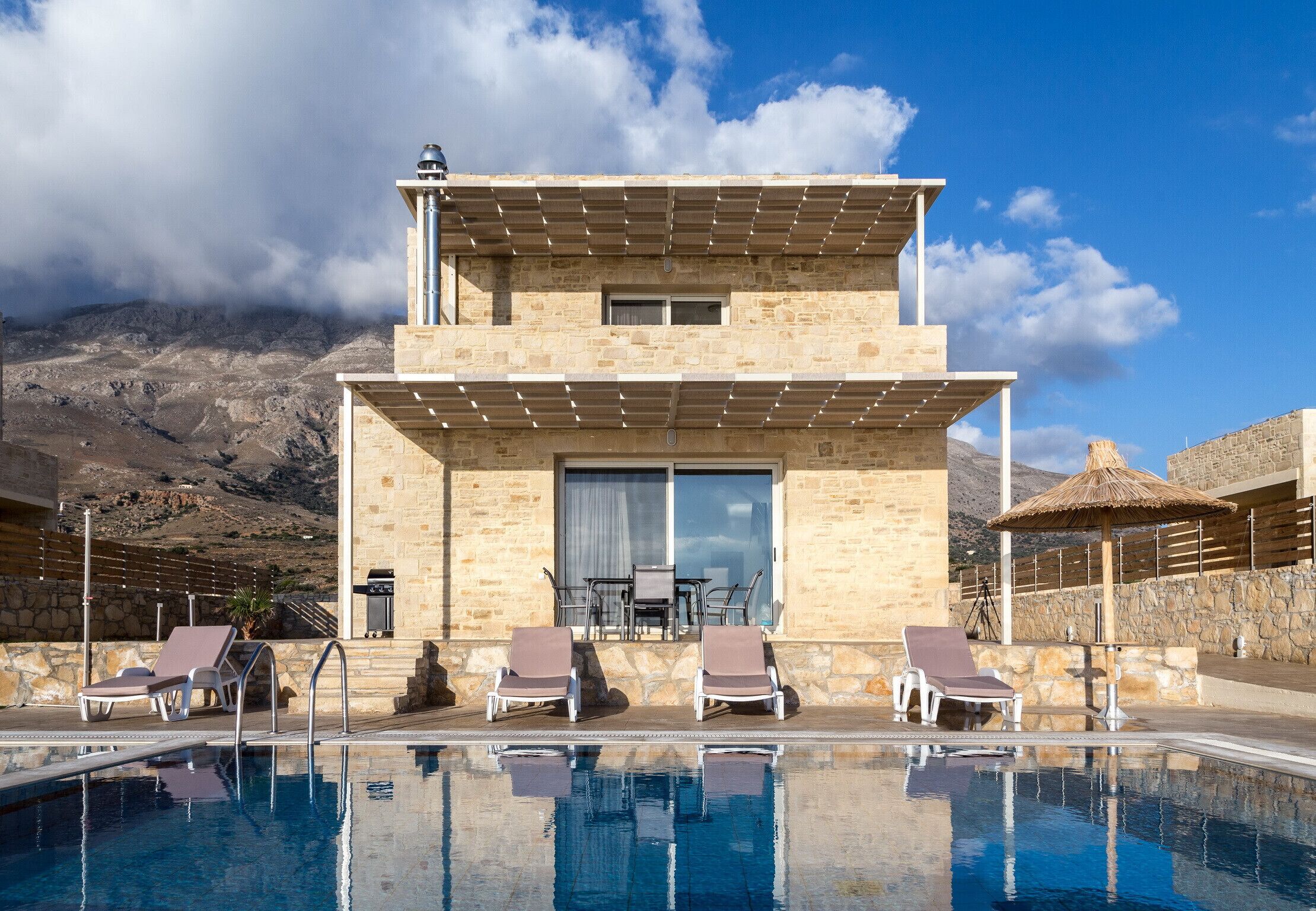 Un hotel moderno con piscina, sillones de descanso y vistas a la montaña.