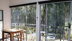 Una habitación con puerta corrediza de vidrio que da a una terraza con mobiliario exterior y vista a un bosque.