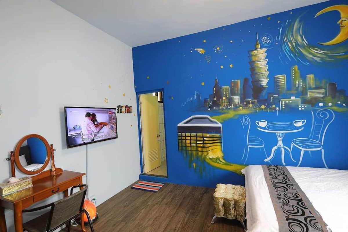A hotel room with a cityscape mural, a TV, a wooden desk, and a bed.