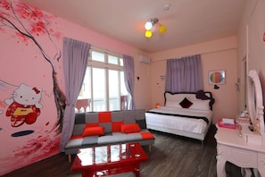 A bedroom with a bed, a sofa, a table, and a wall with a Hello Kitty mural.