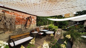 A patio with a wooden bench, tables, and chairs. There is a brick wall with a decorative pattern and a white canopy overhead. - Dům v Centru (Ceska Kamenice)