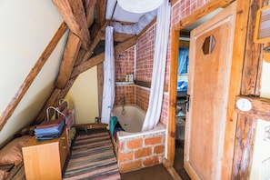 Ein rustikales Badezimmer mit Holzbalkendecke, Ziegelwand, Badewanne und Holztür.