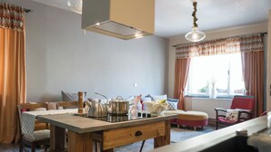 A cozy kitchen with a wooden table, a kettle, a teapot, and a coffee maker. There is a window with curtains and a chair in the background. - Dům v Centru (Ceska Kamenice)
