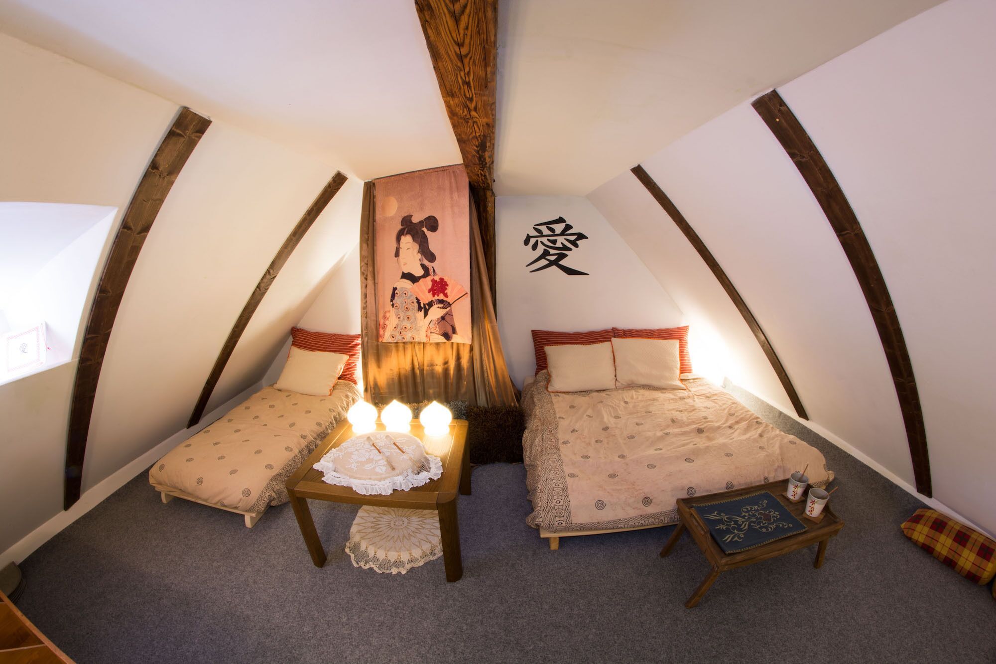 A cozy attic bedroom with two beds, a small table, and a decorative wall hanging.