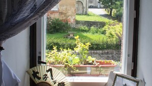 A window with a view of a garden, a fan, and a decorative plate on a wooden ledge. - Dům v Centru (Ceska Kamenice)
