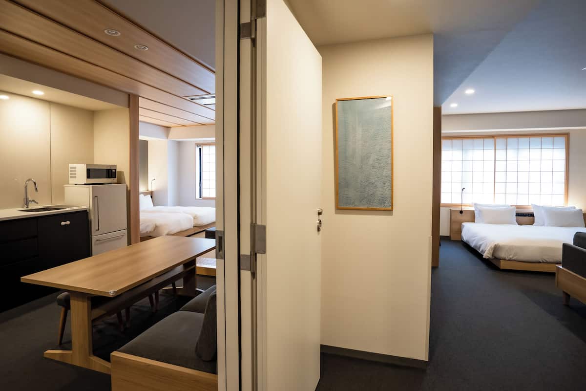 A hotel room with a kitchenette, a bed, a desk, and a large window.
