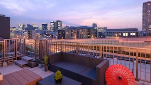 Una terrazza sul tetto con posti a sedere, un ombrello rosso e vista sullo skyline della città.