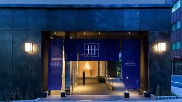 La entrada del Mimaru Apartment Hotel con un diseño moderno, destacando un logotipo prominente y señalización iluminada.