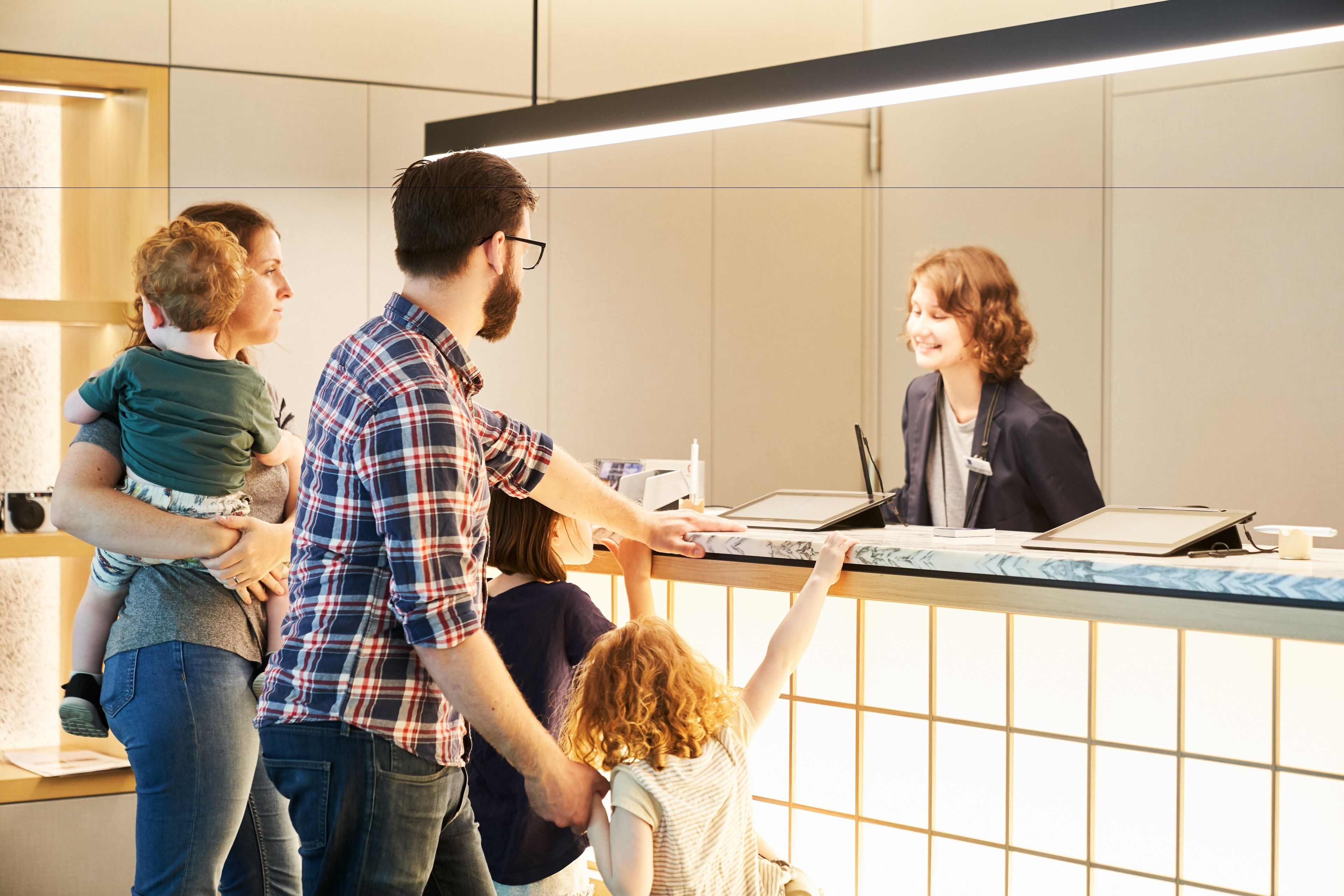 A family interacting with a staff member at a reception desk in a modern hotel lobby.