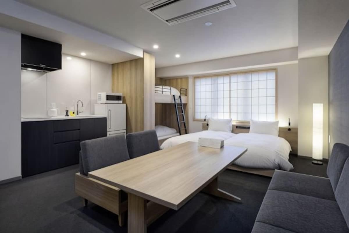 A modern hotel room with a bunk bed, a kitchenette, a dining area, and a large window.