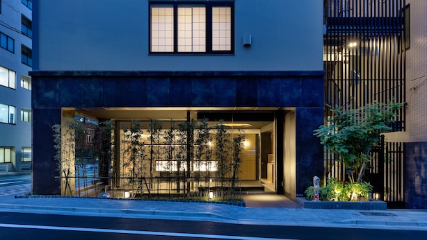 Un edificio moderno con un'ampia entrata, porte in vetro e un piccolo giardino con piante.