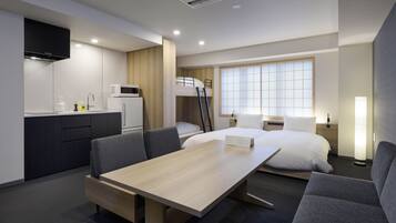 A compact hotel room with a kitchenette, a bed with a ladder, a dining table, and a sofa.
