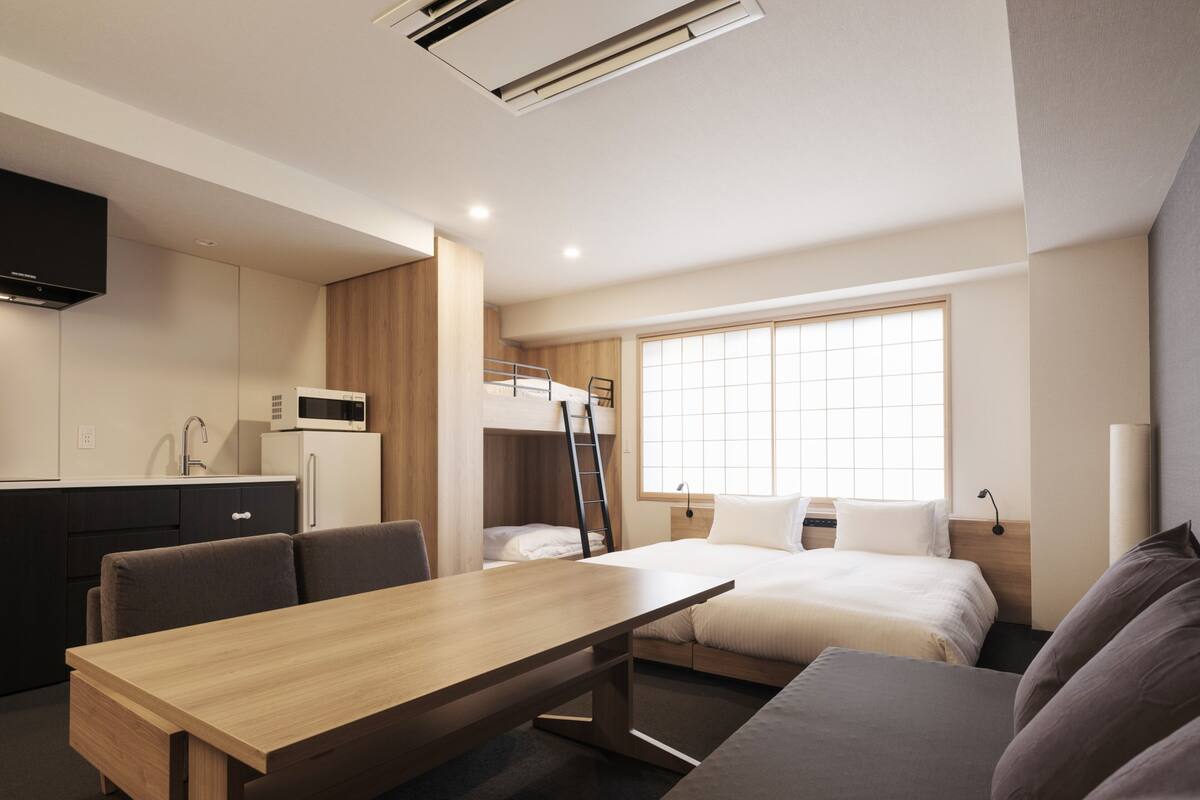 A modern hotel room with a bunk bed, a kitchenette, a dining area, and a large window.