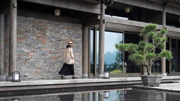 A person walking past a building with a brick wall and a large potted tree. - Tai Chi Hotel (Shiyan)