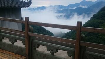Una terraza de madera con barandilla que da a un paisaje montañoso cubierto de niebla y arquitectura tradicional.
