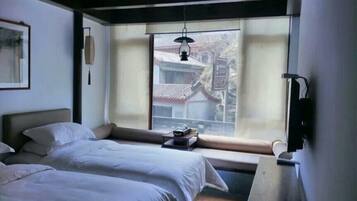 A hotel room with two beds, a window with a view of a traditional building, a hanging light fixture, and a wall-mounted TV.
