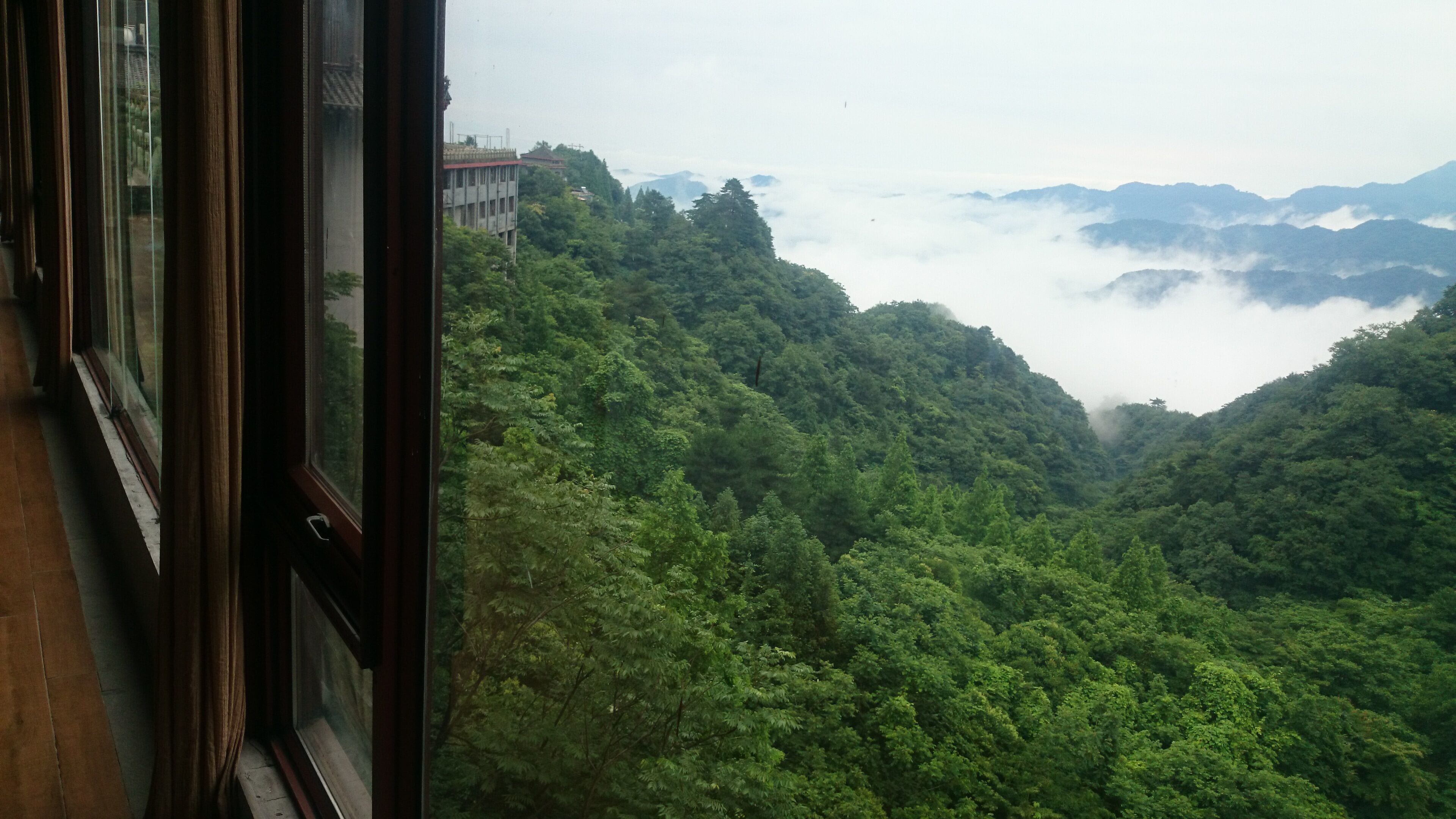 A view from a window overlooking a lush valley with dense greenery and distant mountains.