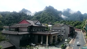 A traditional building with a red roof, surrounded by lush greenery and mountains in the background. - Tai Chi Hotel (Shiyan)