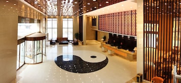 Un vestíbulo amplio con un gran símbolo yin yang blanco y negro en el suelo, un mostrador de recepción y una pared decorativa tradicional china.