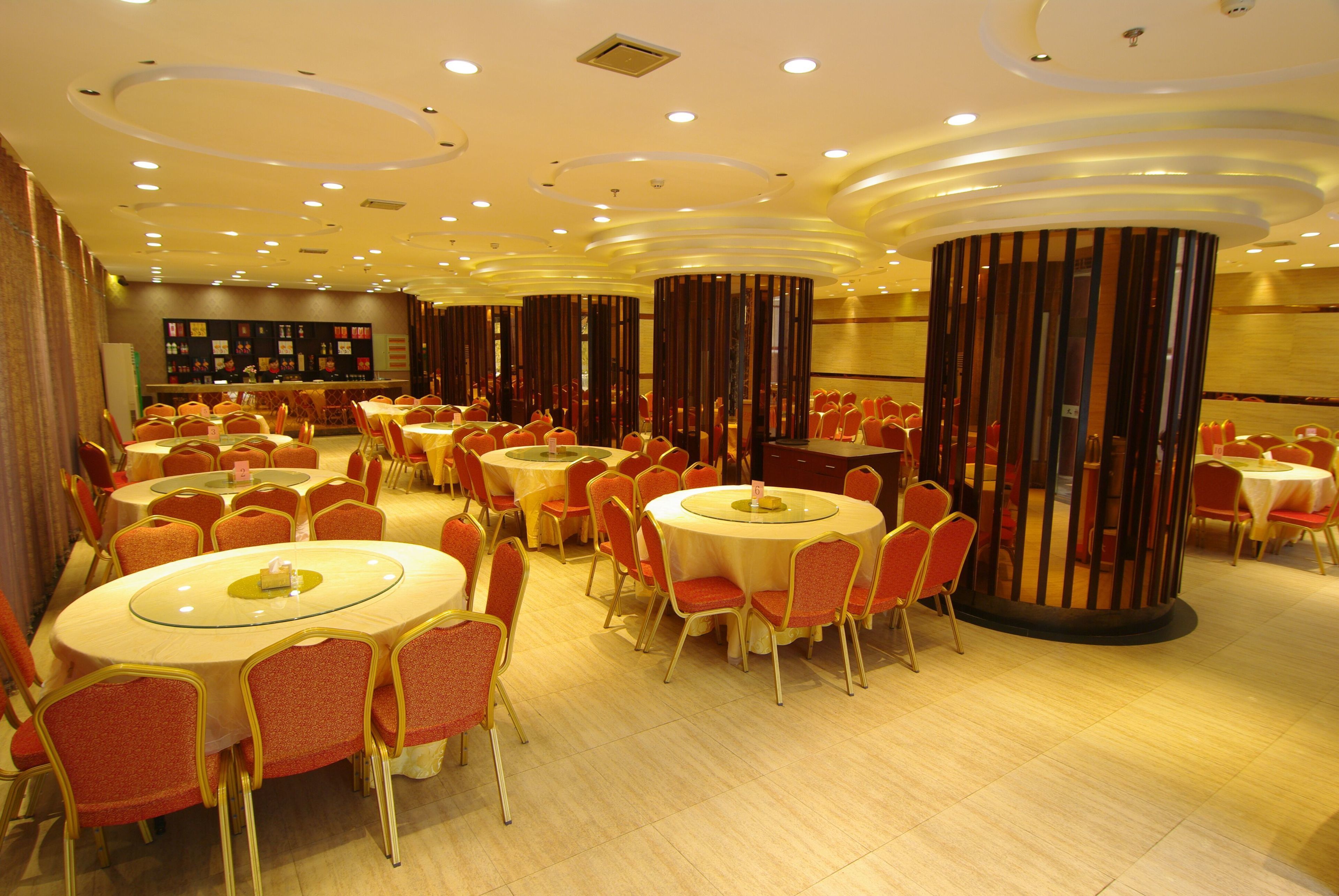Comedor de hotel con mesas redondas y sillas rojas, destacando un diseño de techo moderno y una columna central.