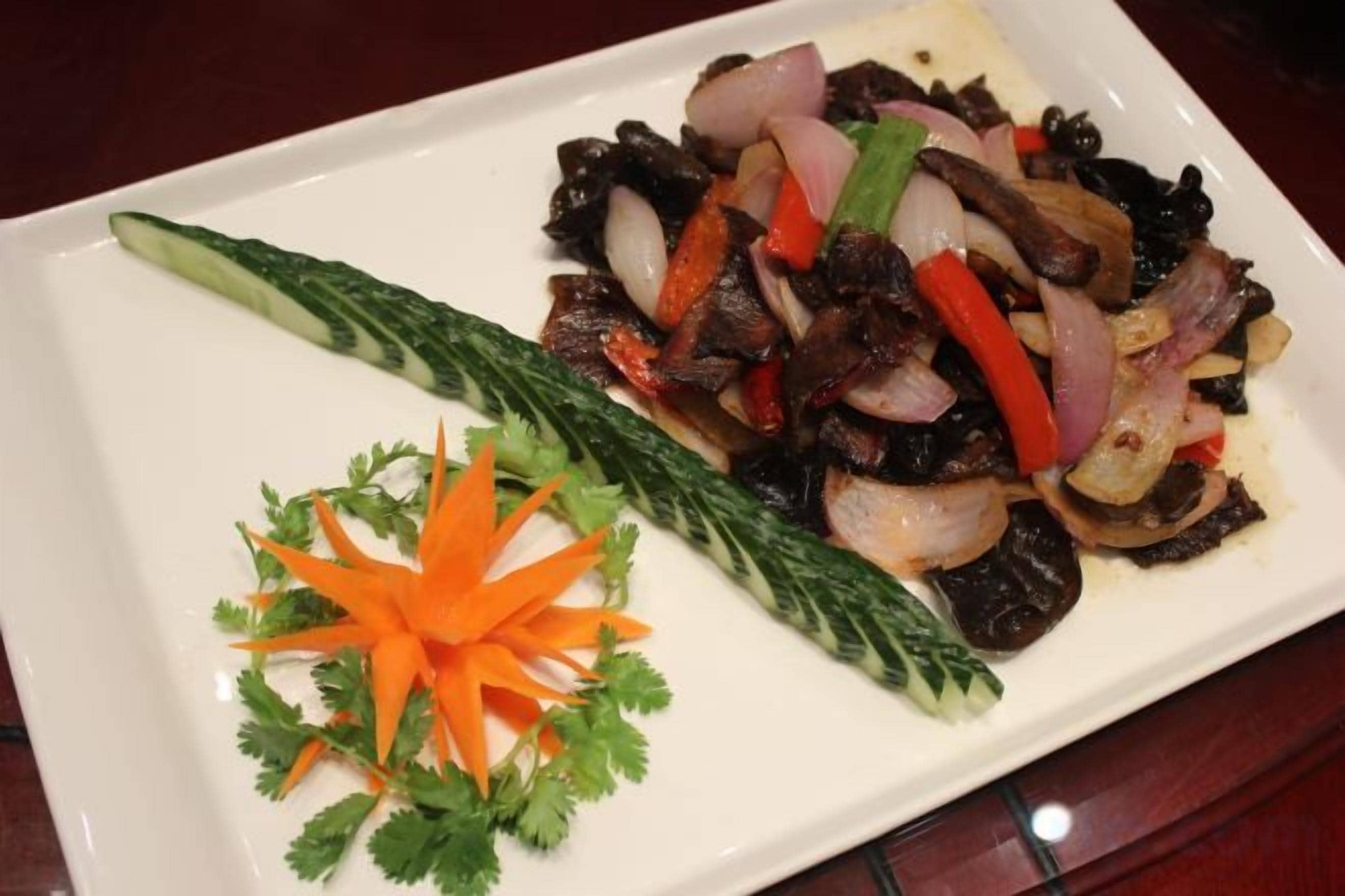 A rectangular plate with a dish of stir-fried meat and vegetables, garnished with a carrot and green herbs.