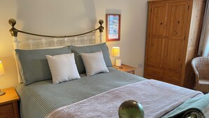 A neatly made bed with a headboard, a wooden wardrobe, and a wicker chair. - Cottage In Dôl Y Bont, Near Aberystwyth, Ceredigion, Wales. (Dol y bont)