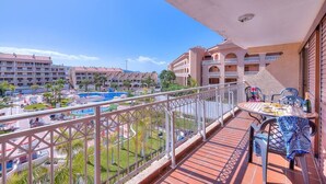 Un balcón con mesa y sillas, con vista a una piscina y edificios de hotel.