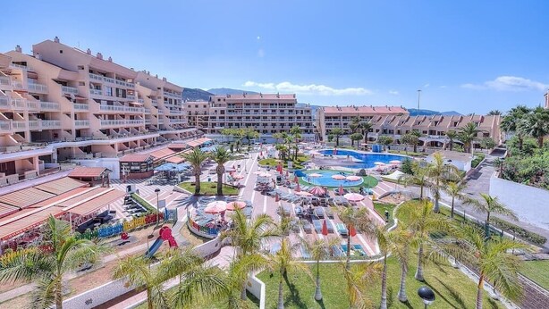 Un hotel con múltiples balcones, piscina y zona de juegos para niños.