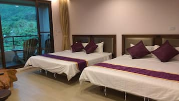 A hotel room with two beds, each with white linens and purple accents, a wooden floor, and a view of greenery through a sliding door.