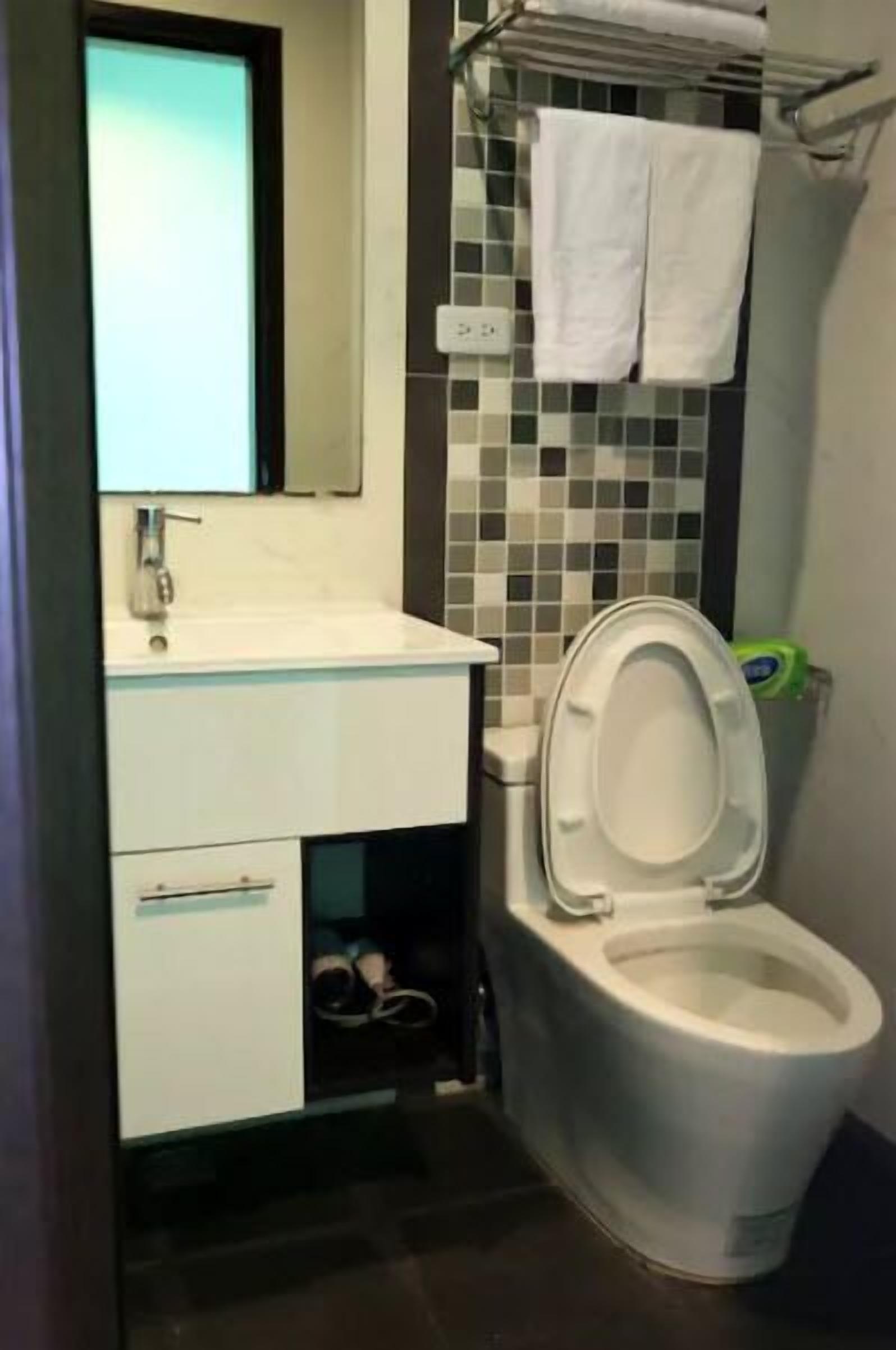 A bathroom with a white toilet, a sink with a mirror above it, and a tiled wall.