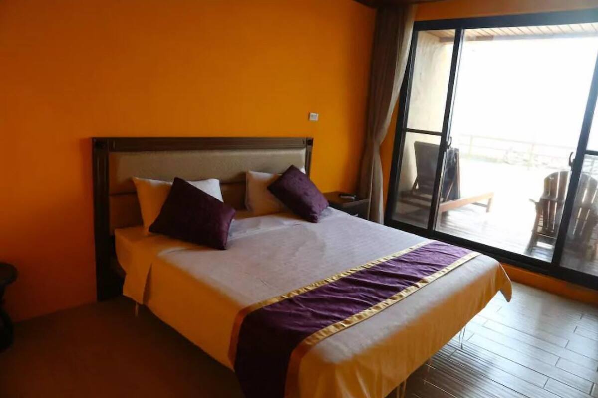 Habitación de hotel con una cama grande, un balcón con sillas y vistas al exterior.