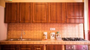 Une cuisine avec des meubles de rangement en bois, un plan de travail recouvert de carreaux, un évier, une machine à café, une bouilloire et une cuisinière.