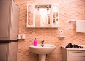 Ein Badezimmer mit einer rosa Seifenfiole, einem weißen Waschbecken und einem Spiegel darüber.