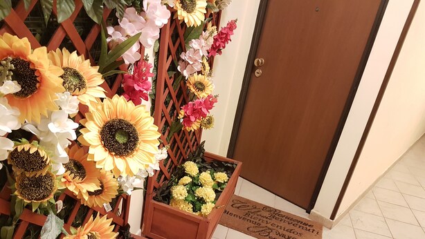 Une porte en bois, un paillasson et une composition décorative de tournesols et de fleurs.