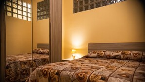 Une chambre d’hôtel avec deux lits, une table de chevet avec une lampe et un grand miroir sur un des murs.