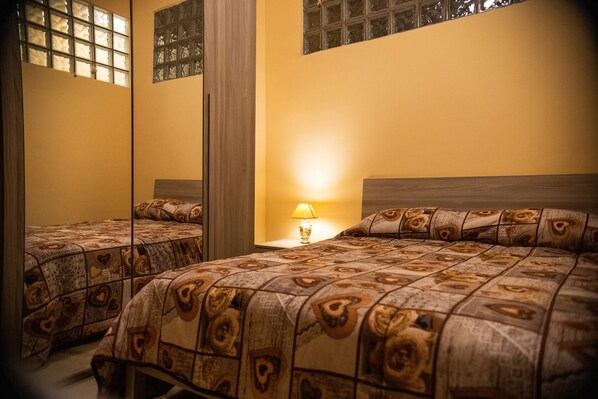 A hotel room with two beds, a nightstand with a lamp, and a large mirror on one wall.