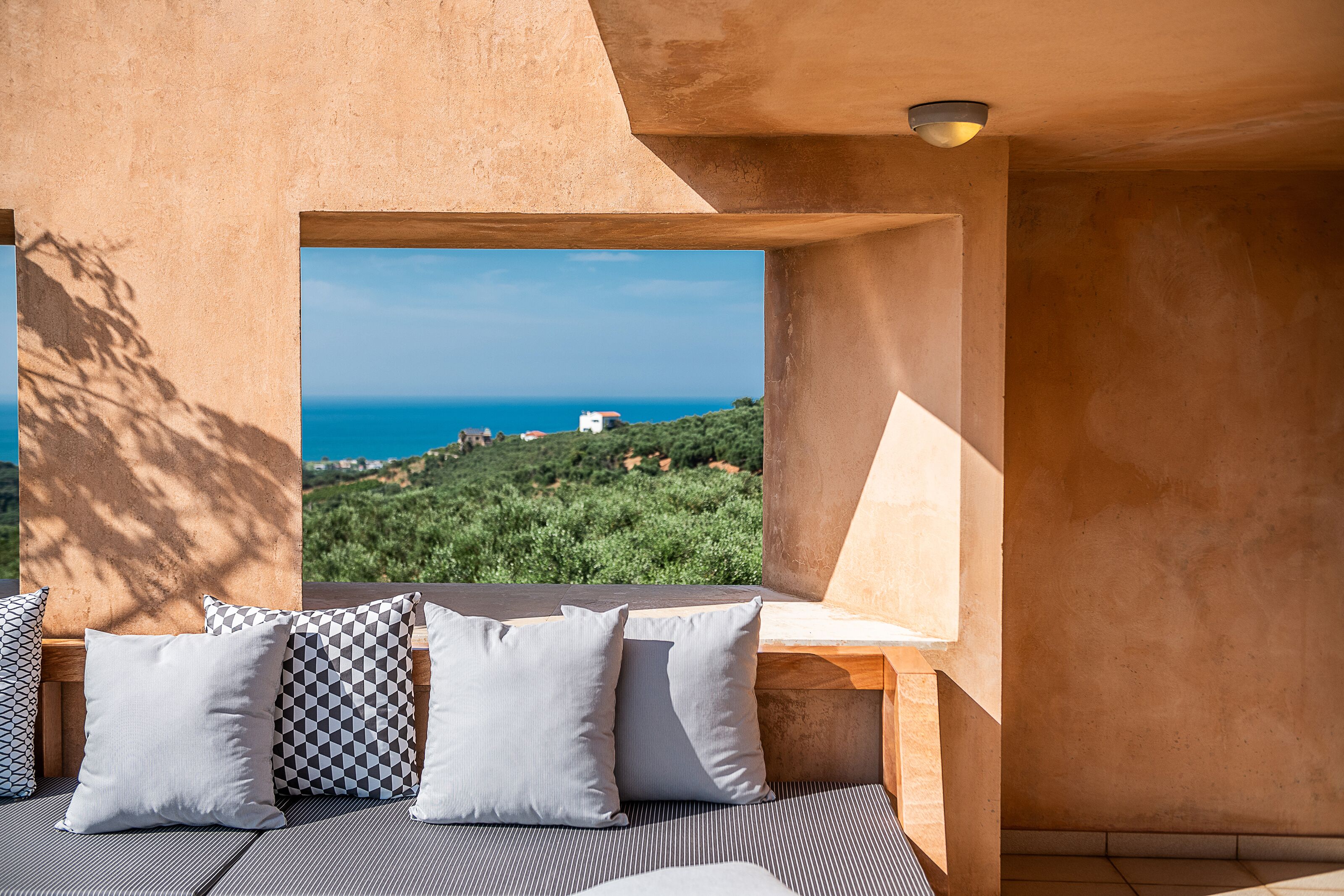 Una habitación con vistas al mar y las colinas, un banco de madera con cojines y una pared con textura.