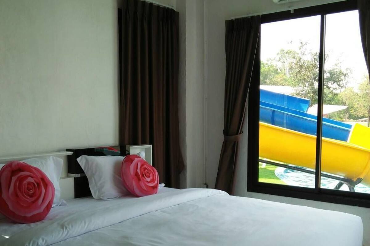 A hotel room with a large bed, white bedding, and a view of a water park through the window.
