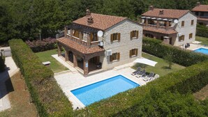 A two-story house with a swimming pool, a covered patio, and a garden.