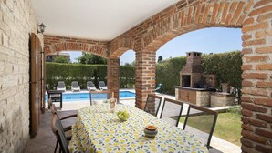 An outdoor patio with a table set for dining, a pool, and a brick barbecue area.